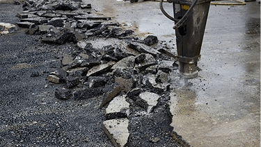 A construction site with broken asphalt pieces and a pavement breaker.