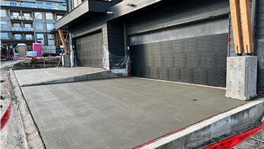 Freshly poured concrete slabs in front of two garage doors at a construction site.