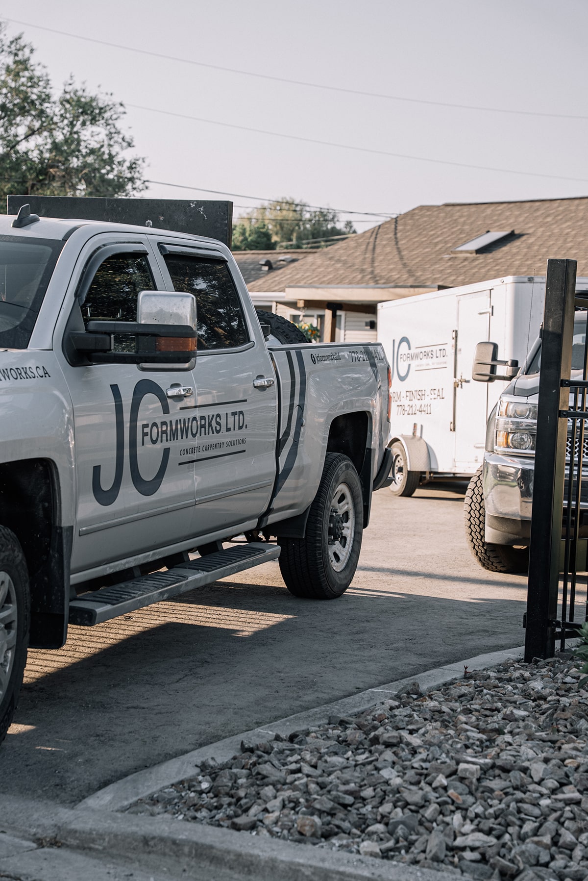 A gray pickup truck with "JC Formworks Ltd." branding parked in a lot, alongside a trailer and another vehicle.
